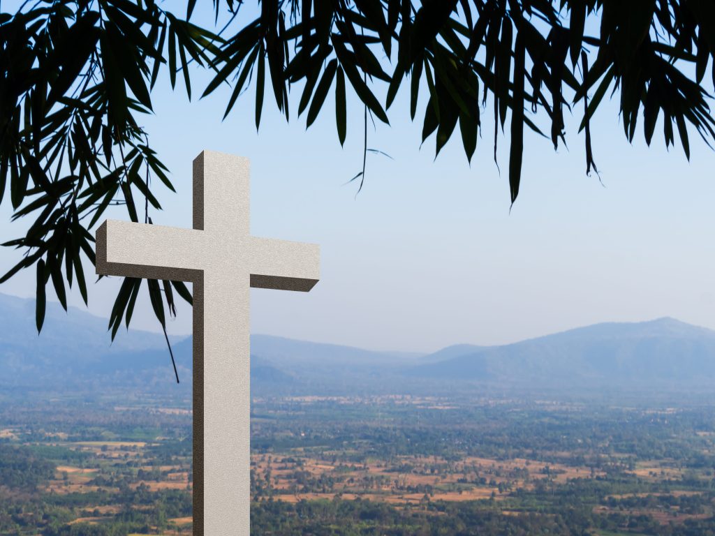 A Christian cross in front of a scenic background.