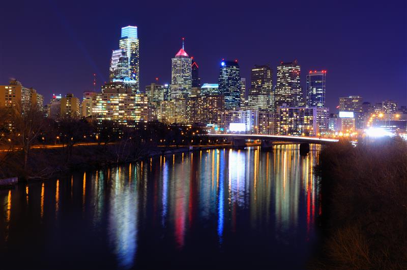 The Philadelphia skyline at night with colorful lights from skyscrapers reflecting off the surface of the Schuylkill River.